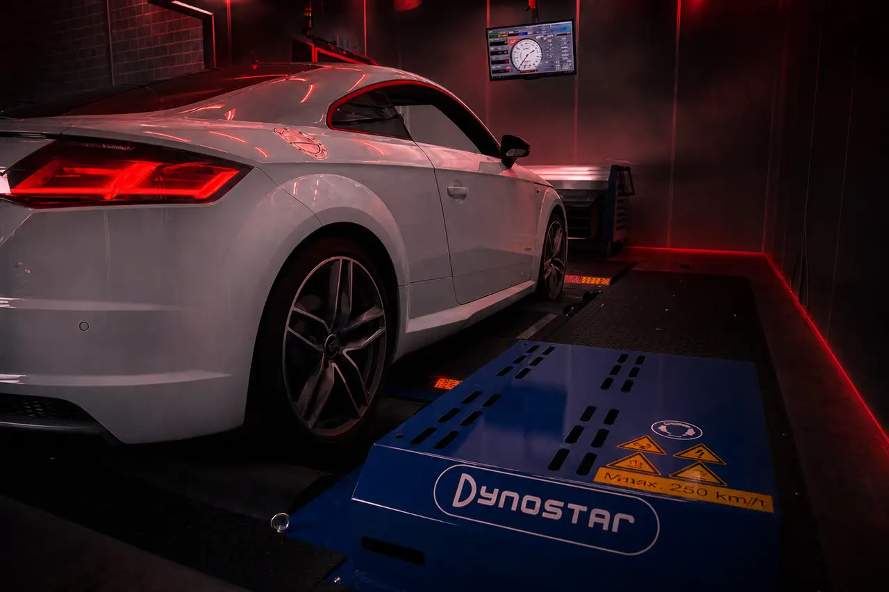 White performance coupe inside a dark red-lit workshop